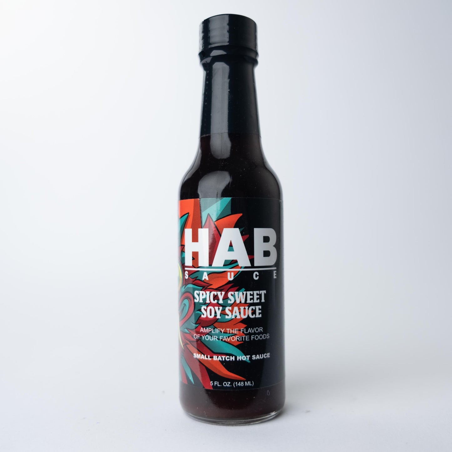 A glass bottle of HAB Spicy Sweet Soy Sauce with a black label, white text, and red and teal graphics, set against a white background.