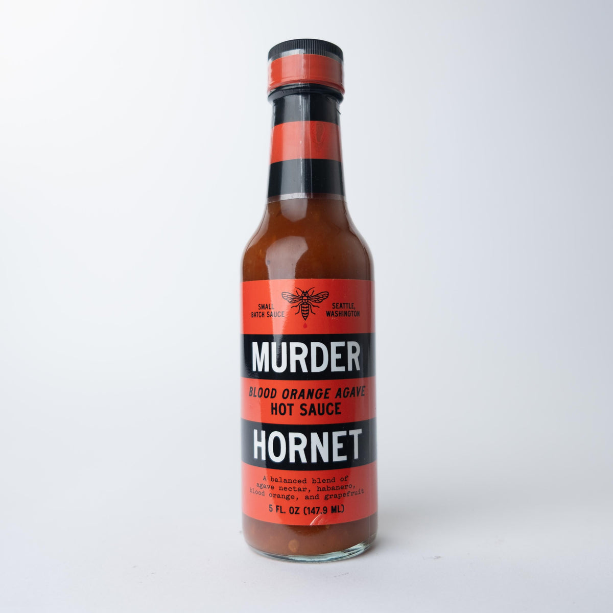 A bottle of Murder Hornet Blood Orange Agave Hot Sauce with a red label, black and white stripes, and a hornet illustration, set against a white background.
